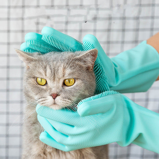 Hand in a teal silicone grooming glove with bristle tips gently brushing a grey cat’s head and neck.